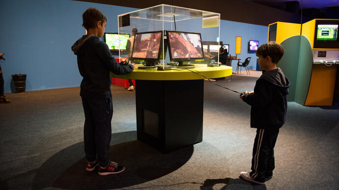 two kids playing a video game inside a glassbox