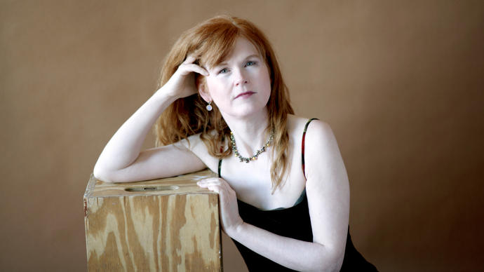 A portrait of Sarah leaning on a wooden plinth 