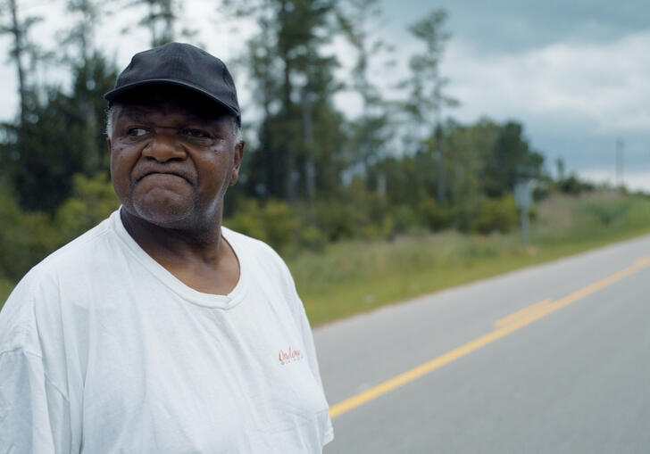 A man wearing a black cap looks down a long road in South Carolina. 
