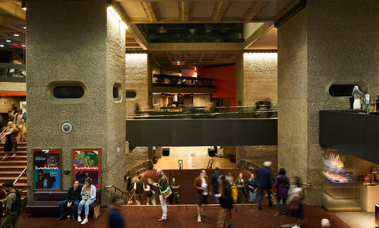 A candid photograph of lots of people sitting or standing in the Barbican Mezzanine foyer