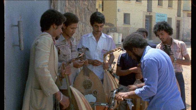 A group of men gather round some instruments on the street in bright sunlight