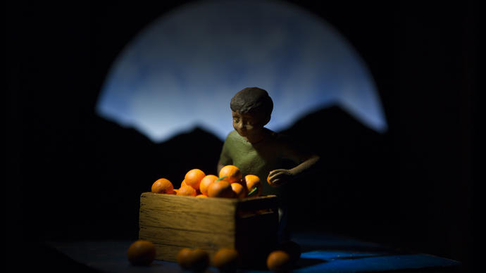 Photo of a boy sitting by a box of oranges