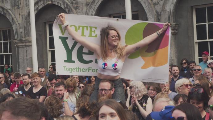 a woman sits on a friend's shoulder at a protest