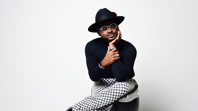 John Holiday smiling, sitting on a stool 