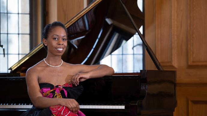 Samantha Ege sits at the piano in a black and pink ballgown