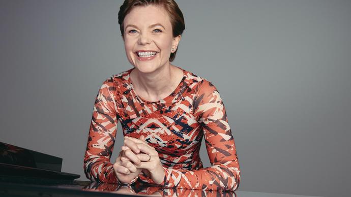 Clare Hammond looks at the camera, sitting at a piano smiling