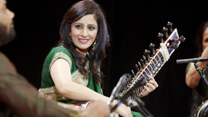 Roopa Panesar on stage playing an instrument smiling 