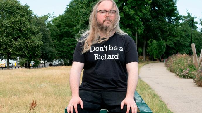 Richard Dawson sitting on a park bench with and ironic t-shirt sloganed with "Don't be a Richard"