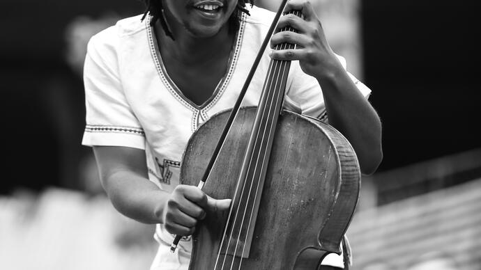 Black and white photo of Abel Selaocoe holding his cello