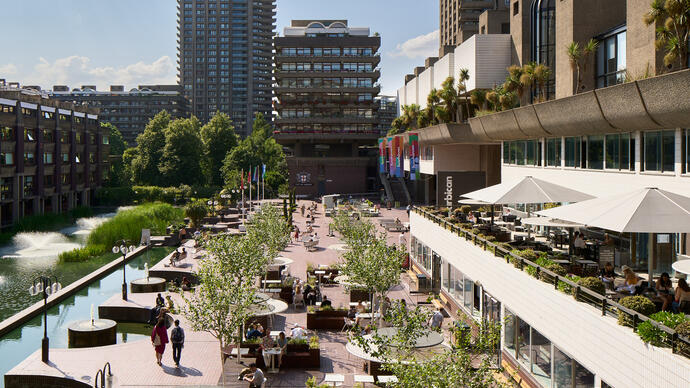 A photo along the Barbican Lakeside in bright sunshine, with a tower at the far end