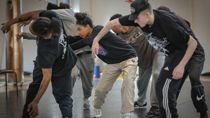 Members of the Boy Blue company rehearse, they stand in a group moving as if spiralling.