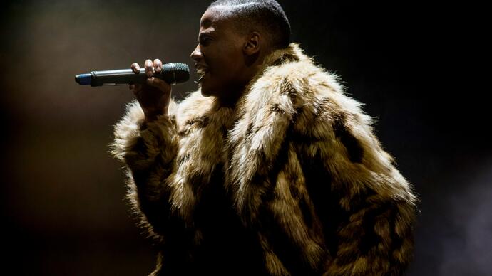 A person in an animal print fur coat sings into a microphone. 