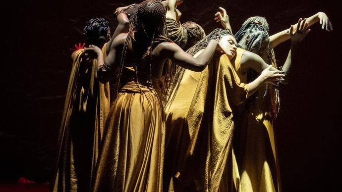 The cast of The Golden Stool performing on stage, wearing long golden dresses