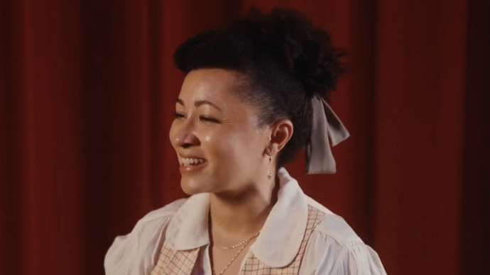 Pamela Phatsimo Sunstrum in front of a red curtain, smiling.