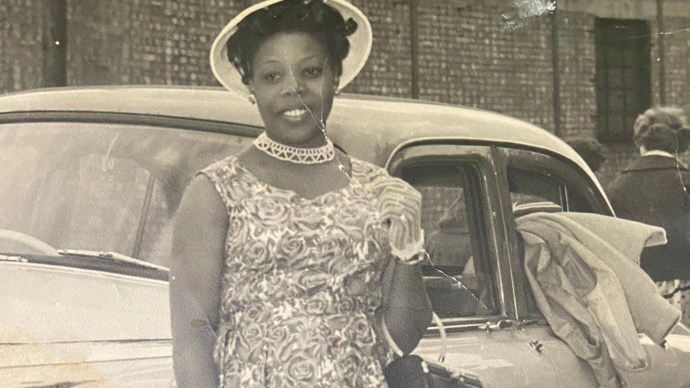 A black and white photograph of a black woman in a floral dress and white hat