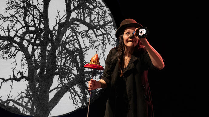 Person in a hat looking through a telescope with a silhouette of a tree against the moon in the background