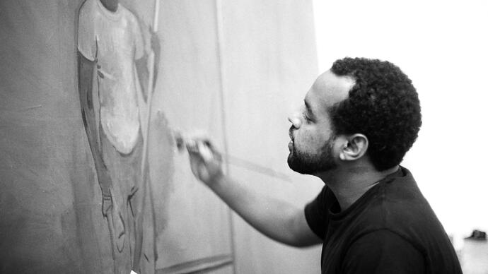 A black and white photo of Noah Davis painting in his studio