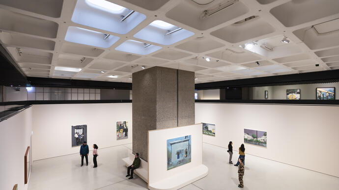 A wide shot of the Noah Davis exhibition in the Art Gallery. People are spread throughout the room, looking at the paintings.