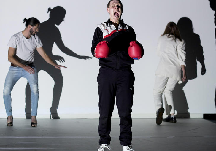 three people on a stage, one wears boxing gloves and screams