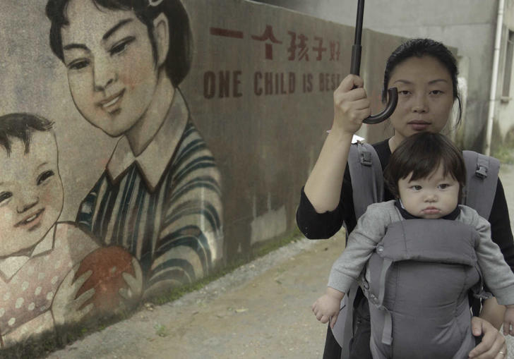 A woman holding her baby in front of a chinese mural