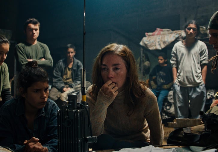 A young woman and some children wait attentively at a radio in the film Monos