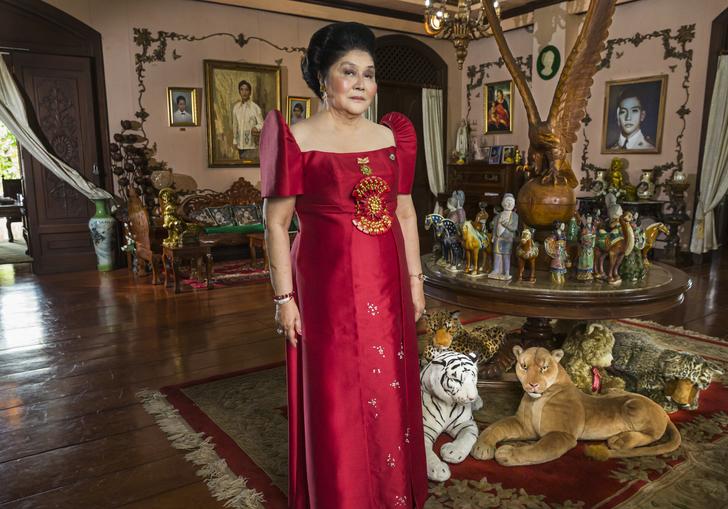 Imelda Marcos standing in an opulent room wearing a red dress