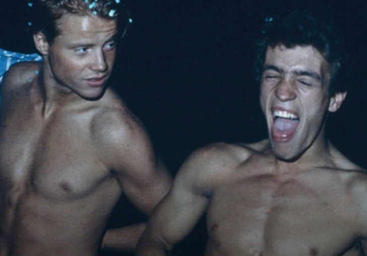 photo of two young topless men laughing in the dark