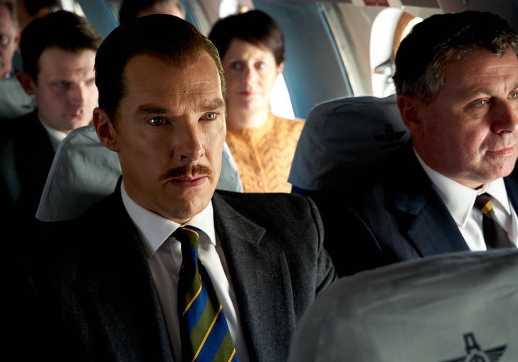 Benedict Cumberbatch sits on a plan wearing a suit