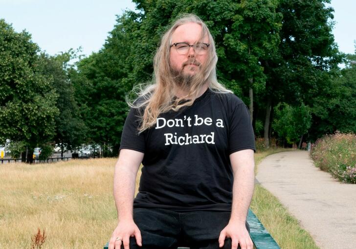 Richard Dawson sitting on a park bench with and ironic t-shirt sloganed with "Don't be a Richard"