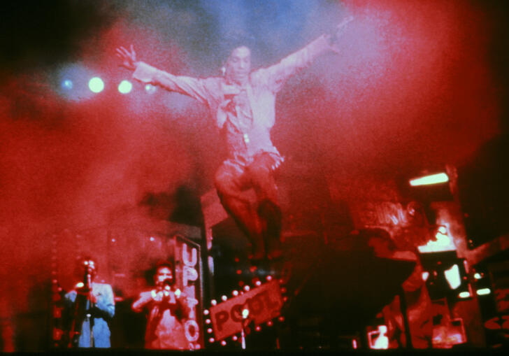 Prince jumps on a stage filled with a red mist. 