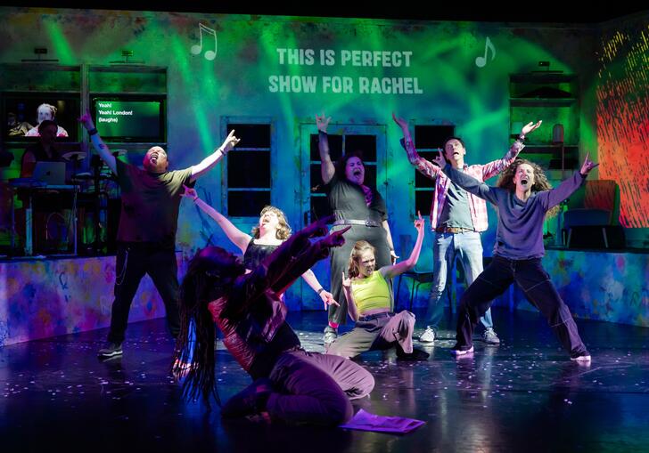 Members of the ZooCo ensemble perform. The move around the stage singing and the words 'This is perfect show for rachel' are projected onto the back wall.