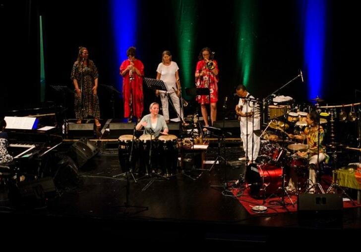 The band play on stage, in multicolour outfits 