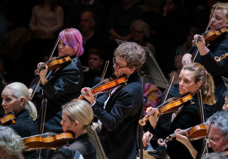 London SymphonyOrchestra string section performing on the Barbican Hall stage.