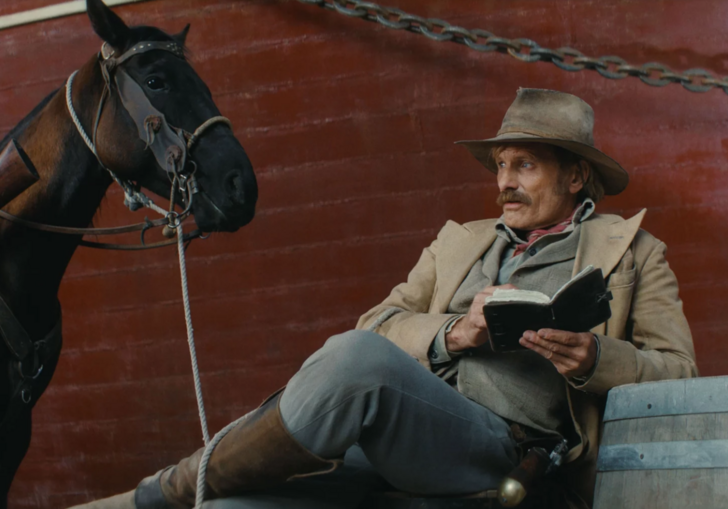 A man is sitting next to a horse in front of a brand. 