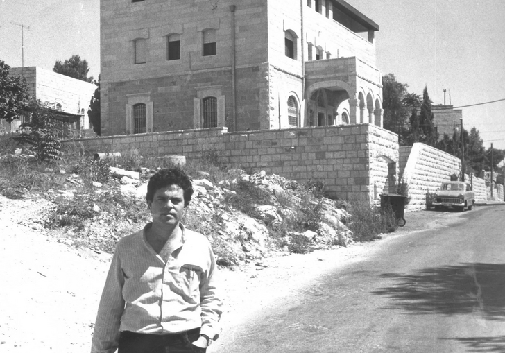 A man stands in front of a new house in the desert.