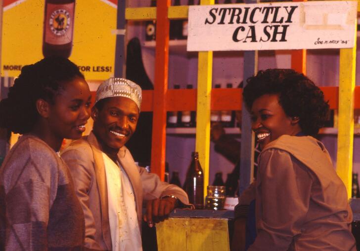 Two women and a man laugh whilst standing in front of a shop front.