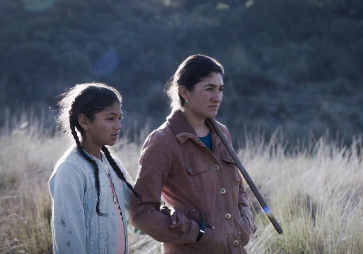 A woman and young girl stand in a field in Mexico, looking out.