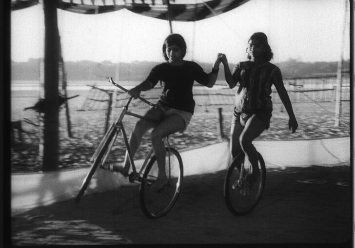 Two women hold hands whilst riding on bicycles.