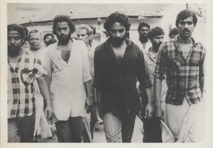 A group of men walk down a street in an aged photograph.