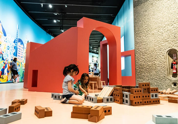 Two young girls sit on the floor in Our Street playing with some building blocks shaped like house bricks.