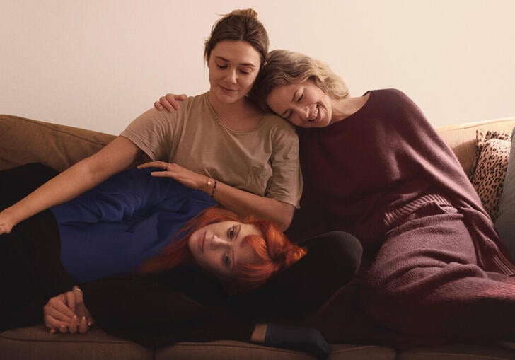 Three sisters sit on a sofa hugging each other. 