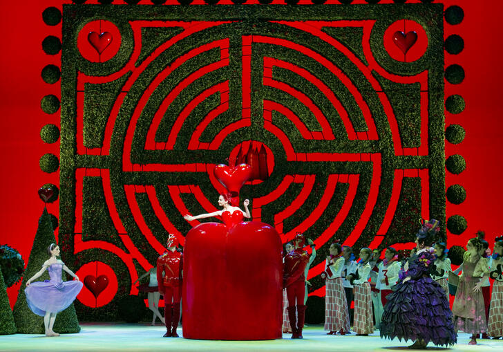 Alice stands in front of a maze whilst the Queen of Heart