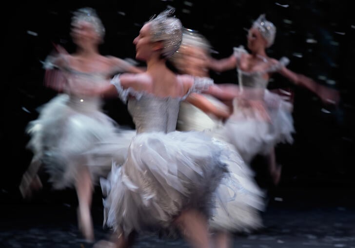 A group of ballet dancers in traditional, fairy-like dress dance around a stage.