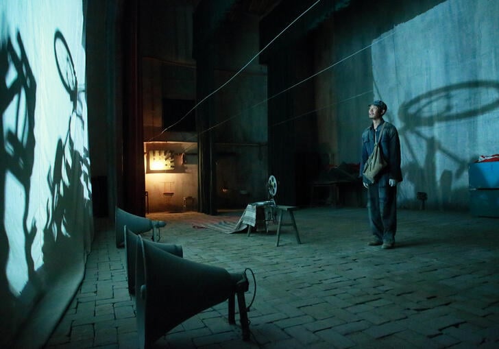 A man stands in front of a bleak room looking at light projected on to a wall.