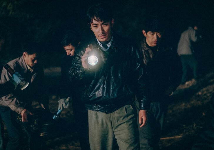 A police man stands with a flashlight in the dark, surrounded by other officers.