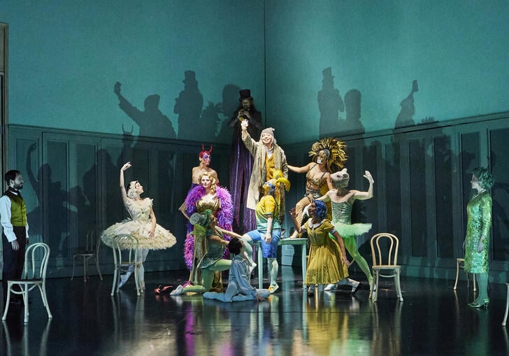 A group of ballet dancers in very colourful clothing pose on a turquoise stage.