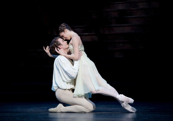 Romeo knees on the ground, holding Juliet intensely in his arms, as they are both in traditional ballet costumes.