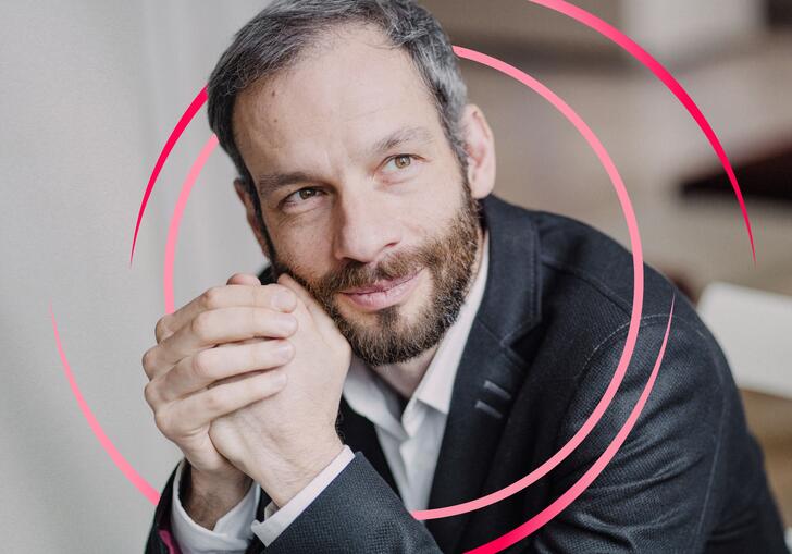 Dima Slobodeniouk clasping his hands in front of his face, with pink circular swirls around him