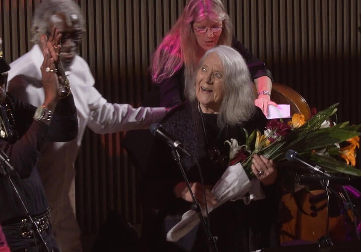 Barbara is holding a bunch of flowers surrounded by other musicians 