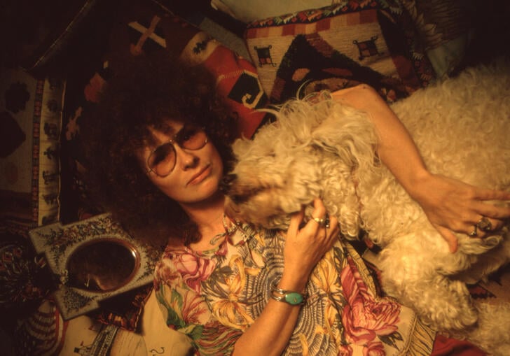 Dory Previn lies down surrounded by cushions and hugging a white dog